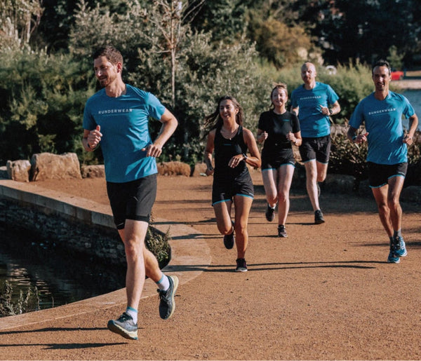A single image of 5 people in runderwear branded t-shirts running along a path next to a body of water